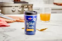 A container of Swanson Sipping Chicken Bone Broth on countertop with glass of broth in background