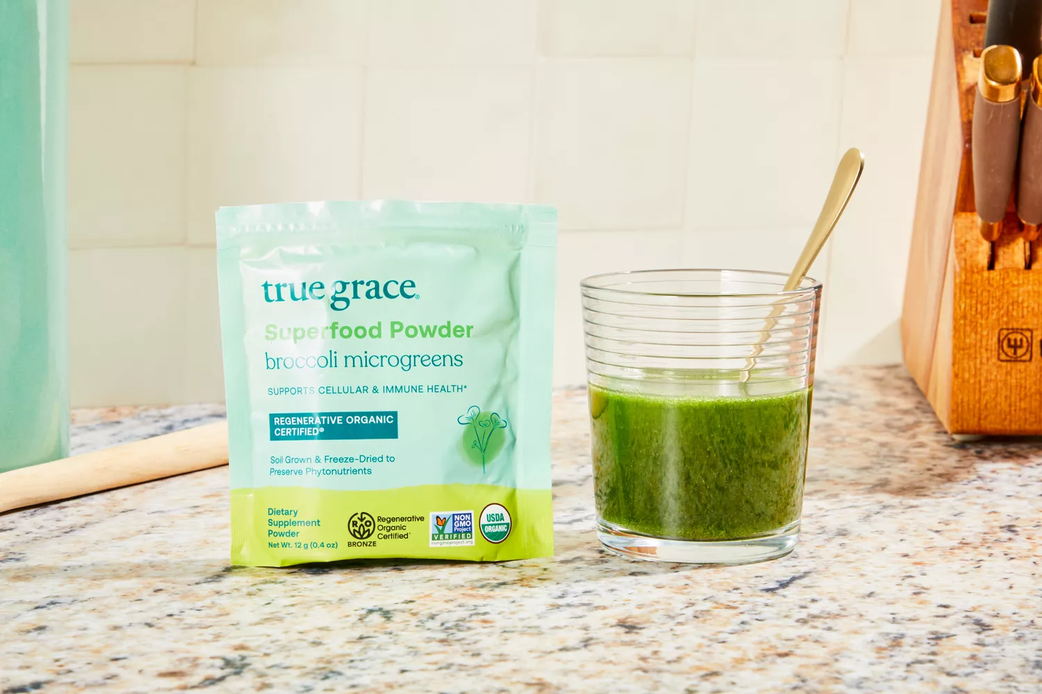True Grace Superfood Powder Broccoli Microgreens displayed on speckled counter mixed in a glass of water next to its packaging