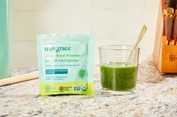 True Grace Superfood Powder Broccoli Microgreens displayed on speckled counter mixed in a glass of water next to its packaging
