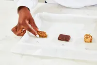 A hand touching a small rectangular item labeled A on a parchment surface with two other labeled items B and C nearby