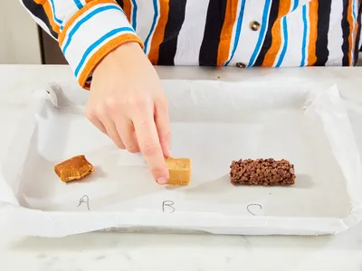 A hand reaches to touch one of three food samples labeled A B and C on a tray