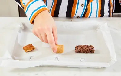 A hand reaches to touch one of three food samples labeled A B and C on a tray