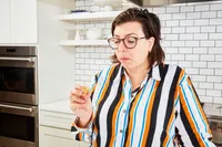 Person in a kitchen tasting food while holding a small piece in hand