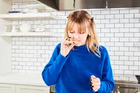 Person in kitchen holding a food item appearing to examine or smell it