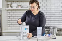 A person removes a scoop of Klean Athlete Klean Isolate Protein Powder from the bag