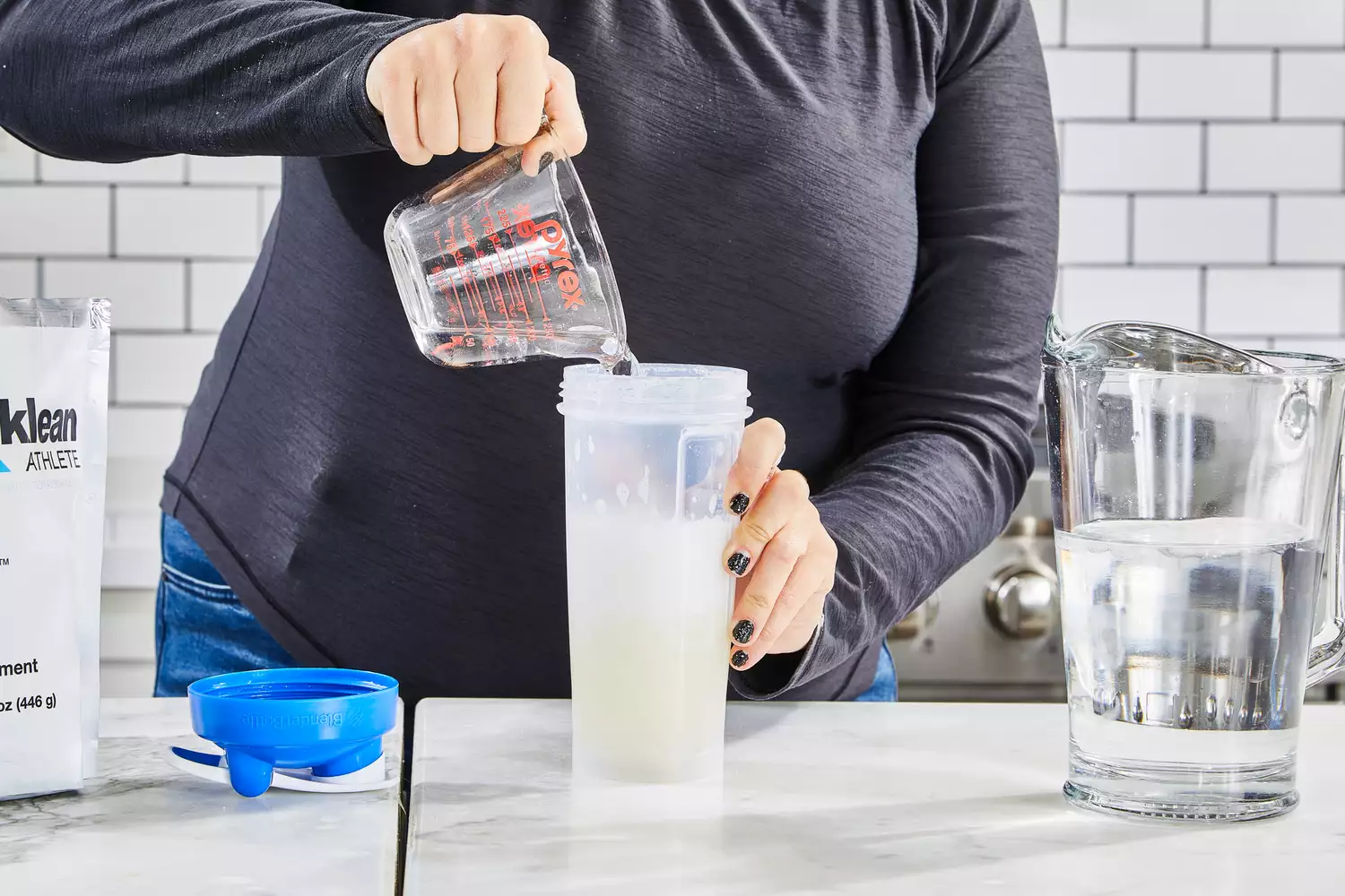 A person pours water into Klean Athlete Klean Isolate Protein Powder