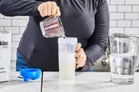 A person pours water into Klean Athlete Klean Isolate Protein Powder