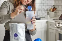 Person adding Ritual Essential Protein Daily Shake 50+ to a protein shaker