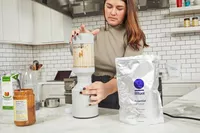 Person blending a smoothie next to Ritual Essential Protein Daily Shake 50+ 