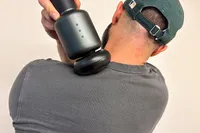 A person uses the Rally Massage Gun on their shoulder
