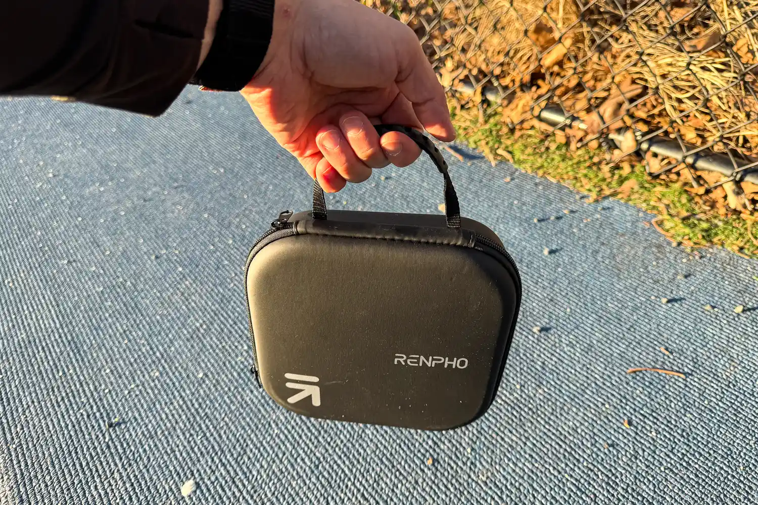 A person carries the Renpho Mini Thermal Massage Gun by the handle on the storage case