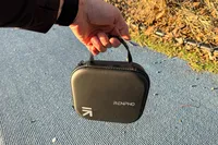 A person carries the Renpho Mini Thermal Massage Gun by the handle on the storage case