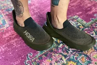 A person wearing Hoka Restore TC Recovery Shoes on a rug