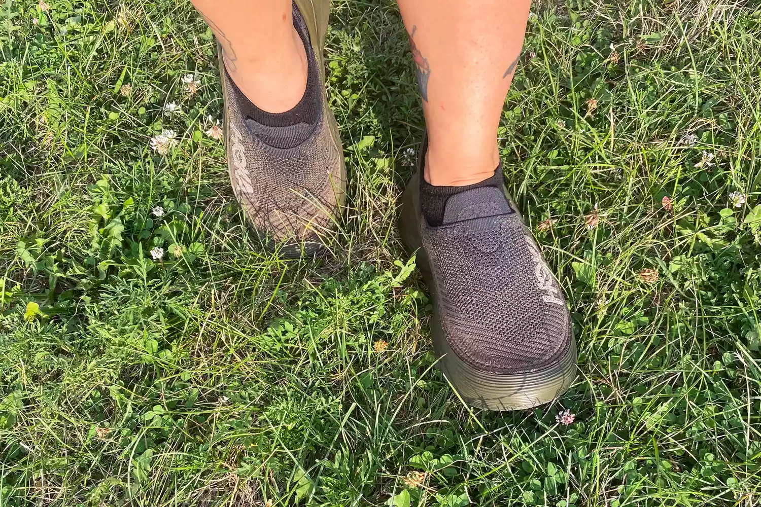 A person wearing Hoka Restore TC Recovery Shoes in the grass