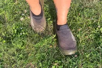 A person wearing Hoka Restore TC Recovery Shoes in the grass