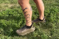 A person standing on grass while wearing the Hoka Restore TC Recovery Shoes