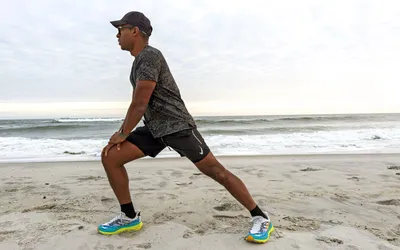 A person stretching on a beach while wearing Hoka Women's Stinson 7