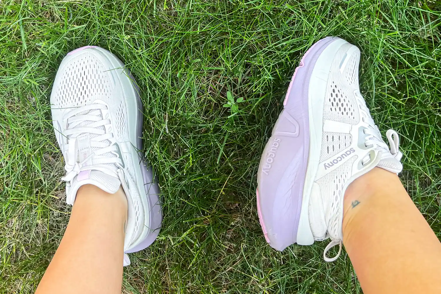 Two feet wearing the Saucony Women's Guide 18 Sneakers on grass