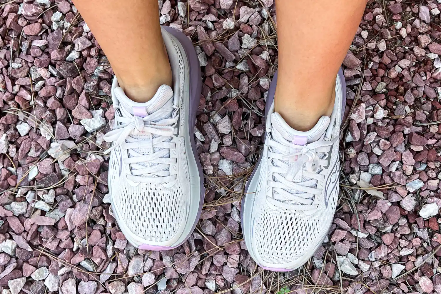 Two feet wearing the Saucony Women's Guide 18 Sneakers on pebbles
