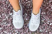 Two feet wearing the Saucony Women's Guide 18 Sneakers on pebbles