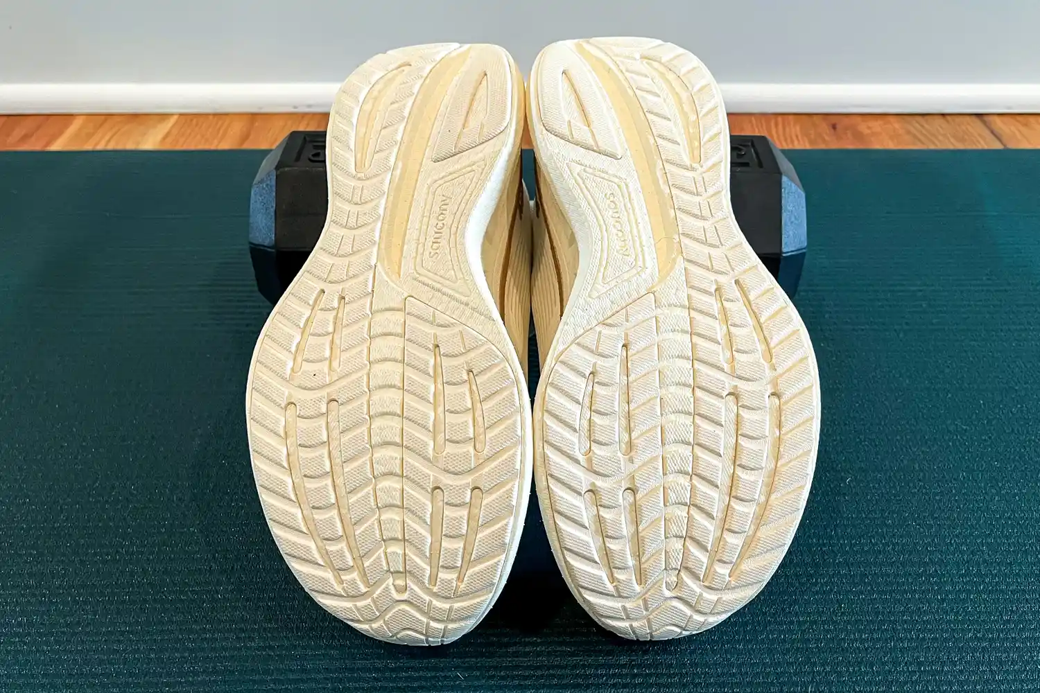The soles of a pair of athletic shoes positioned on a dark exercise mat