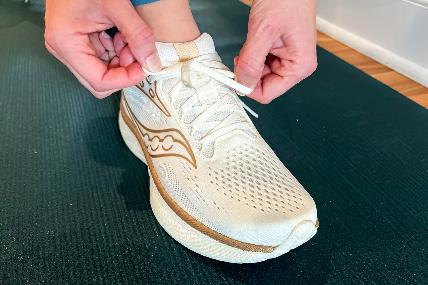 Hands tying the laces of a running shoe on a ridged mat
