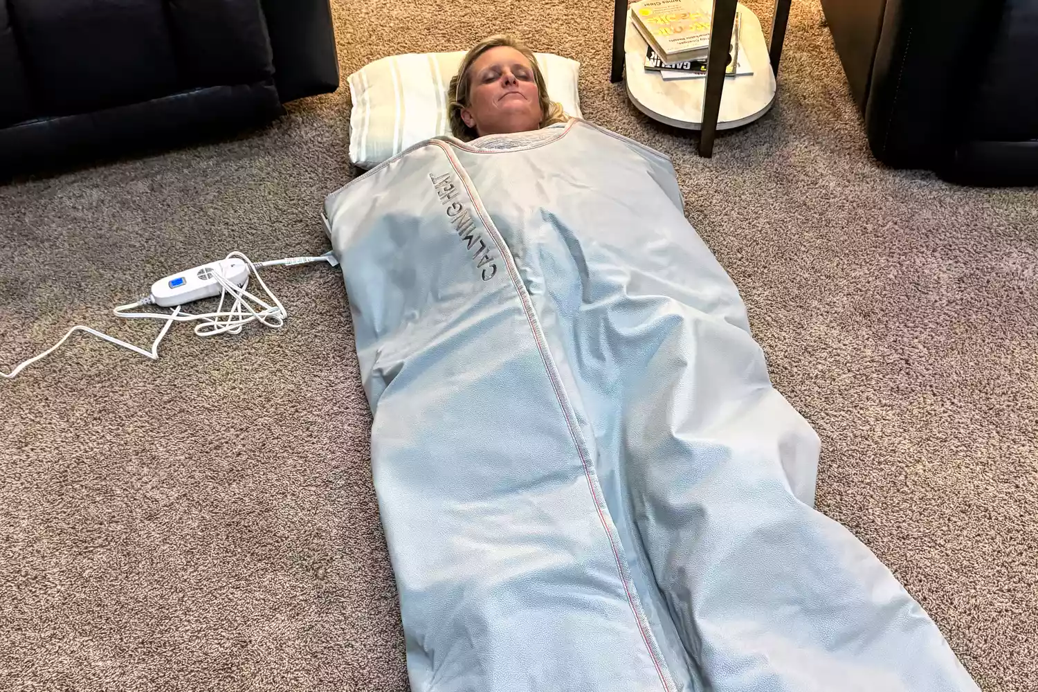 A person using the Sharper Image Calming Heat Sauna Infrared Wrap placed on a carpet near furniture
