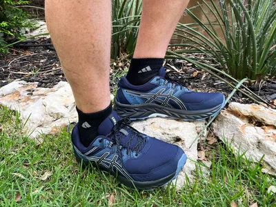 Feet wearing Asics Gel Venture 7 Shoes on rocks and grass