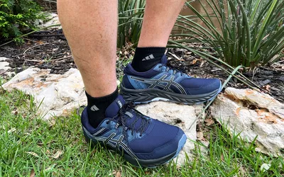 Feet wearing Asics Gel Venture 7 Shoes on rocks and grass