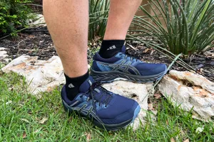 Feet wearing Asics Gel Venture 7 Shoes on rocks and grass