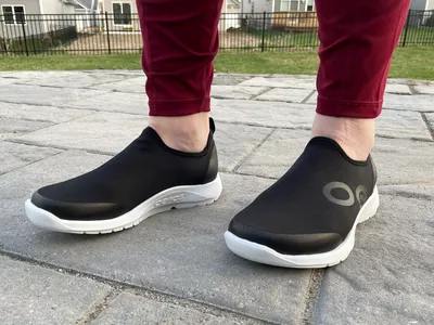 Feet wearing a pair of OOFOS OOmg Sport Low Shoes outside