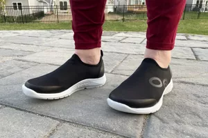 Feet wearing a pair of OOFOS OOmg Sport Low Shoes outside