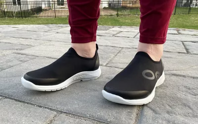 Feet wearing a pair of OOFOS OOmg Sport Low Shoes outside