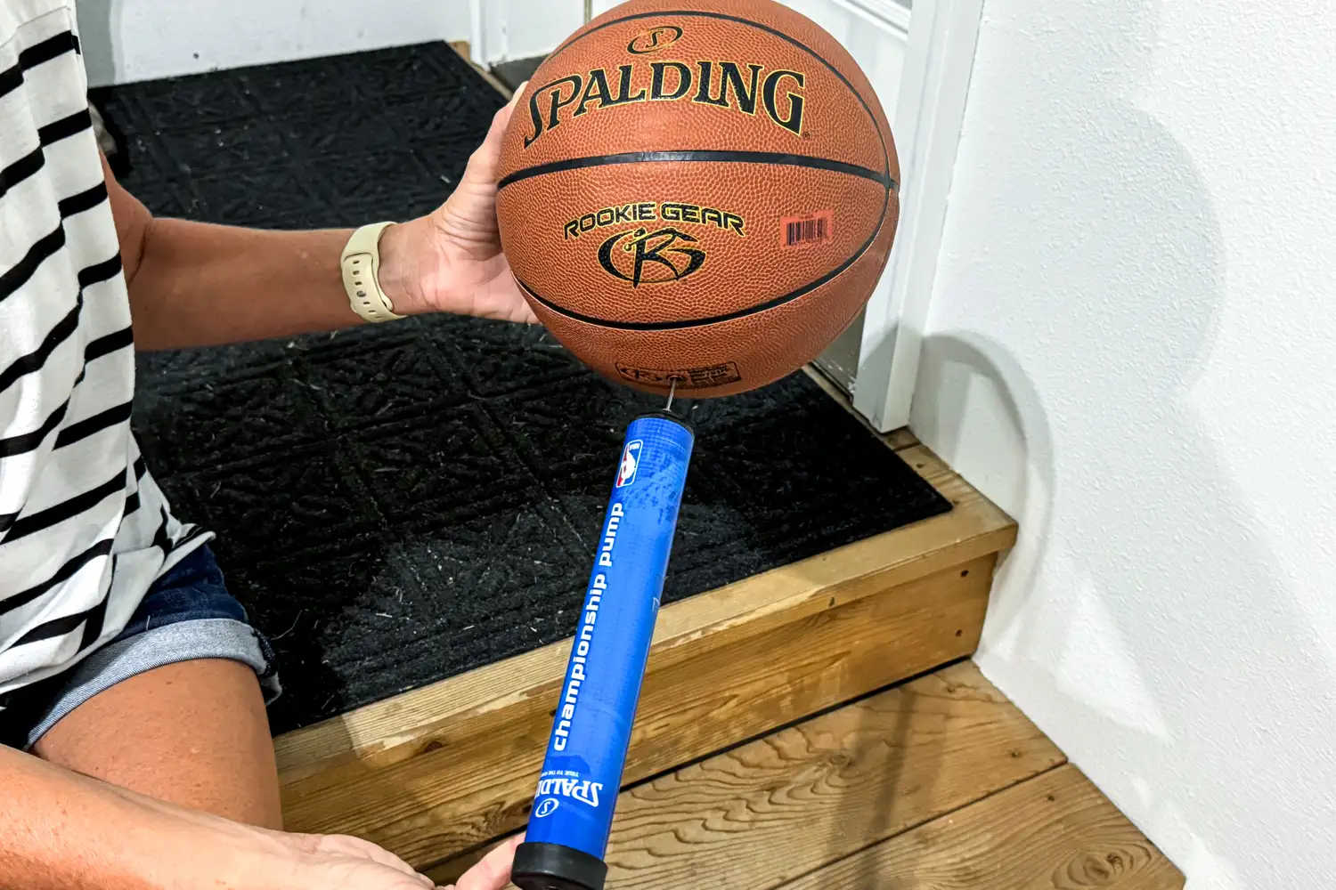 A person pumps air into the Spalding Rookie Gear Youth Indoor-Outdoor Basketball
