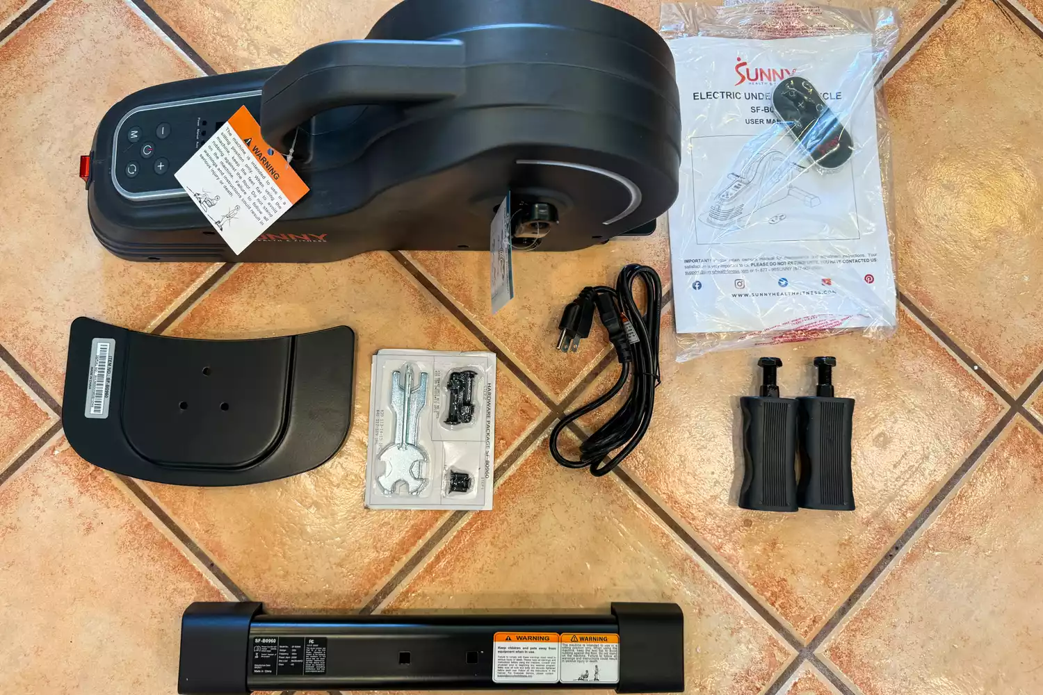 The pieces of the Sunny Health & Fitness SF-B0960 Motorized Electric Under Desk Bike on a tile floor