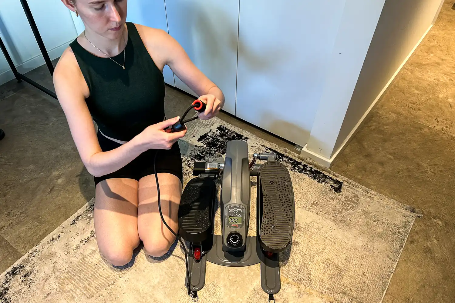 A person examines the handle on the Sunny Health & Fitness Smart Stand/Sit Mini Elliptical Exercise Trainer arm strap