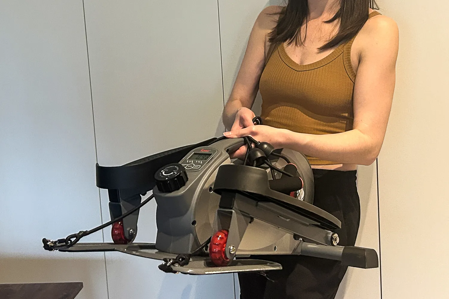 A person lifts the Sunny Health & Fitness Smart Stand/Sit Mini Elliptical Exercise Trainer