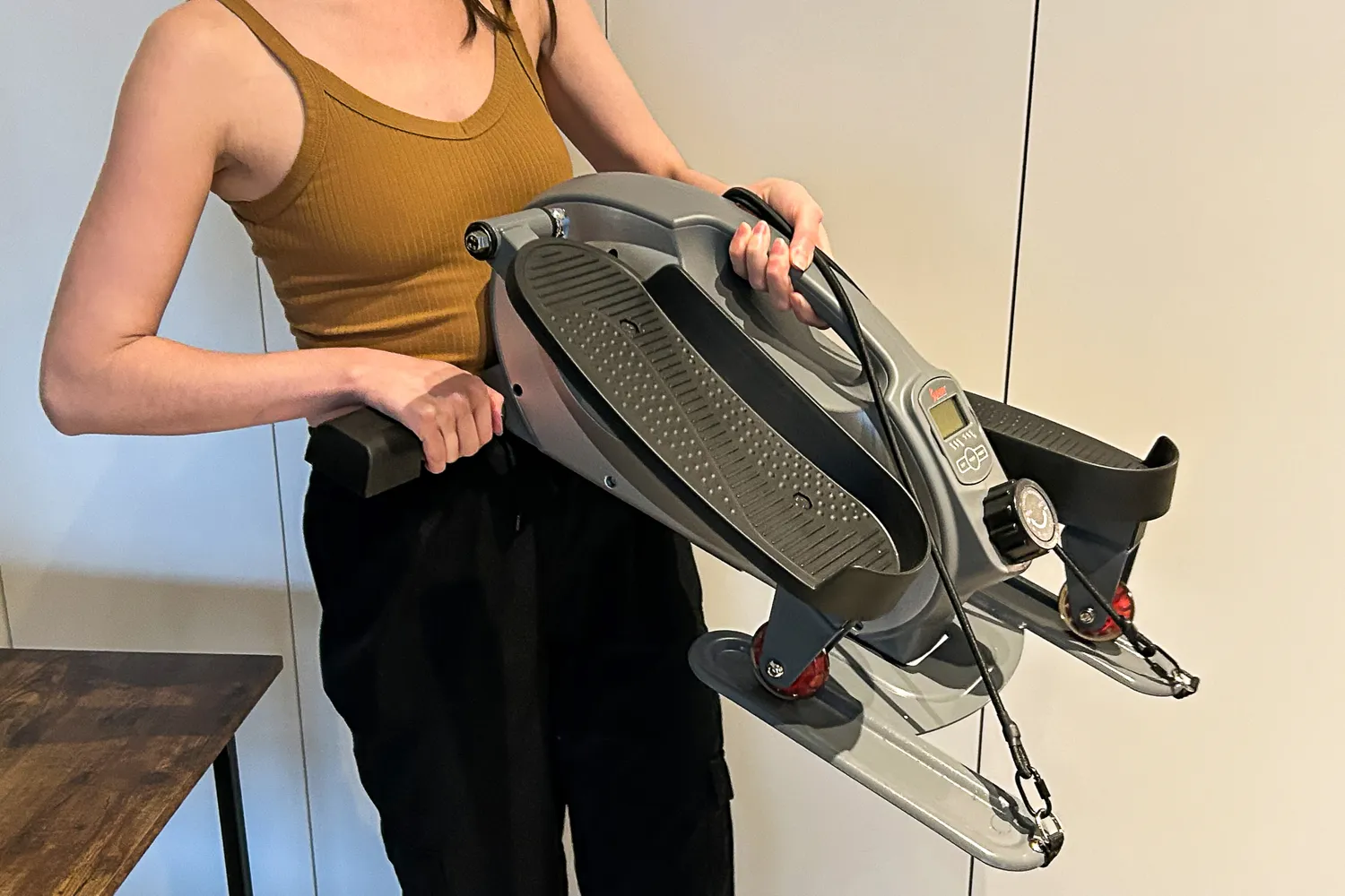 A person lifts up the Sunny Health & Fitness Smart Stand/Sit Mini Elliptical Exercise Trainer