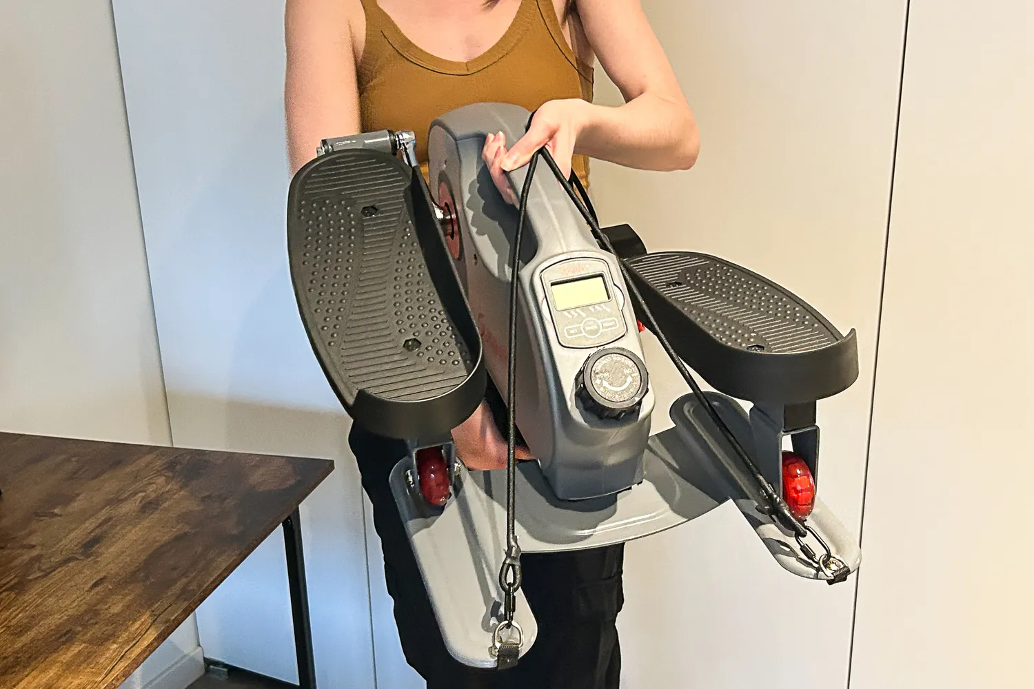 A person lifts up the Sunny Health & Fitness Smart Stand/Sit Mini Elliptical Exercise Trainer