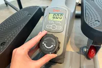 A person turns the tension control dial on the Sunny Health & Fitness Smart Stand/Sit Mini Elliptical Exercise Trainer