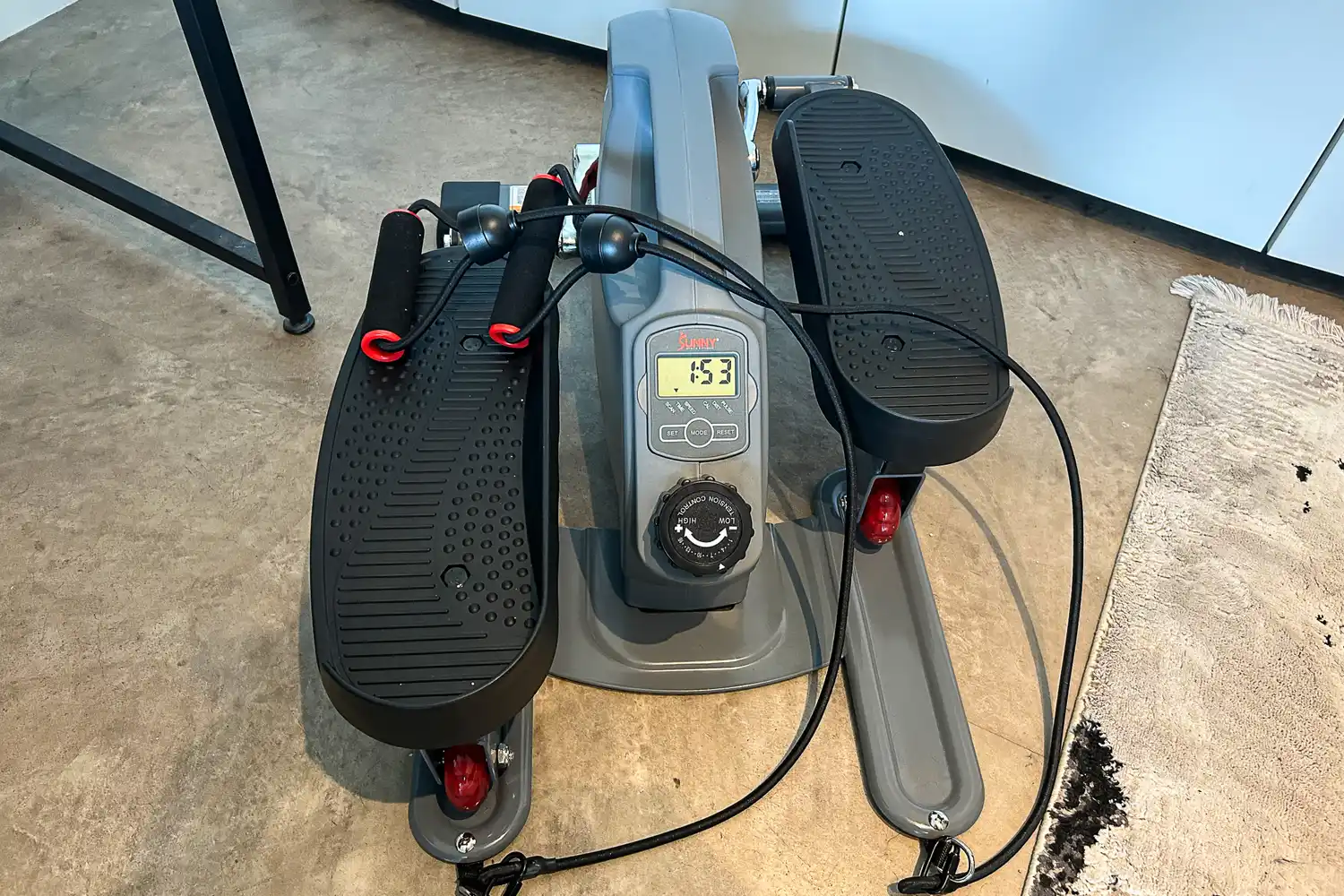 The Sunny Health & Fitness Smart Stand/Sit Mini Elliptical Exercise Trainer on a concrete floor