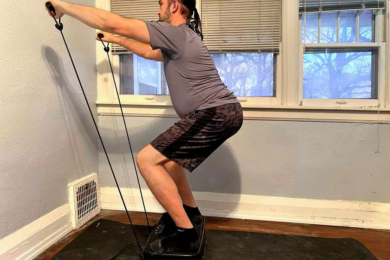 A person pulls the resistance bands on the Sunny Health & Fitness Fitboard 2D Vibration Platform With Resistance Band