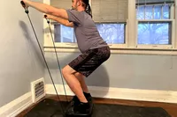 A person pulls the resistance bands on the Sunny Health & Fitness Fitboard 2D Vibration Platform With Resistance Band