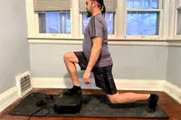 A person does lunges on the Sunny Health & Fitness Fitboard 2D Vibration Platform With Resistance Band