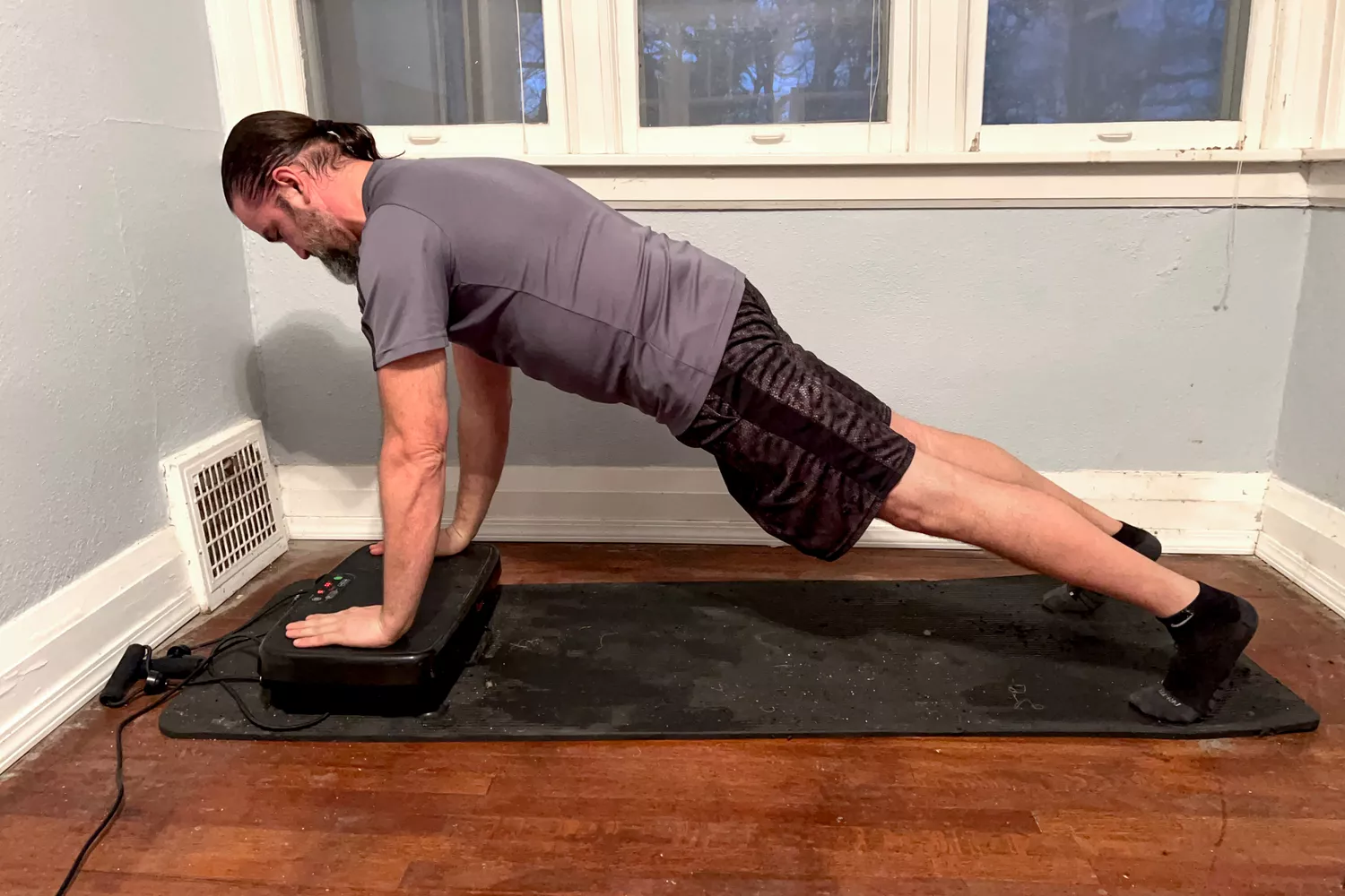 A person does pushups on the Sunny Health & Fitness Fitboard 2D Vibration Platform With Resistance Band