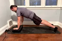 A person does pushups on the Sunny Health & Fitness Fitboard 2D Vibration Platform With Resistance Band