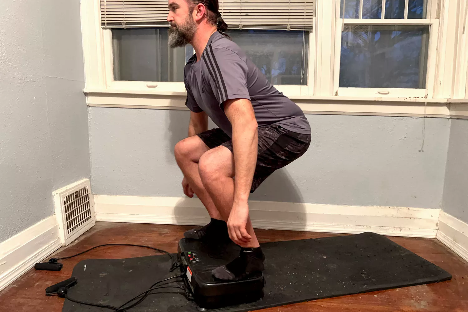 A person squats on the Sunny Health & Fitness Fitboard 2D Vibration Platform With Resistance Band