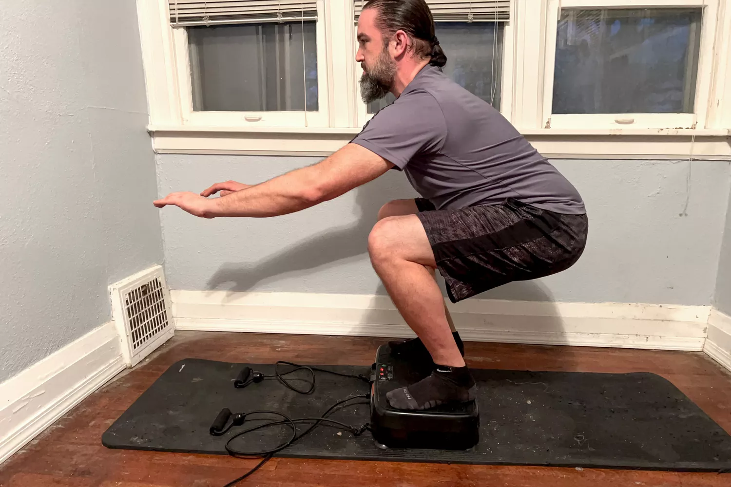 A person squats on the Sunny Health & Fitness Fitboard 2D Vibration Platform With Resistance Band