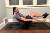 A person does ab exercises on the Sunny Health & Fitness Fitboard 2D Vibration Platform With Resistance Band