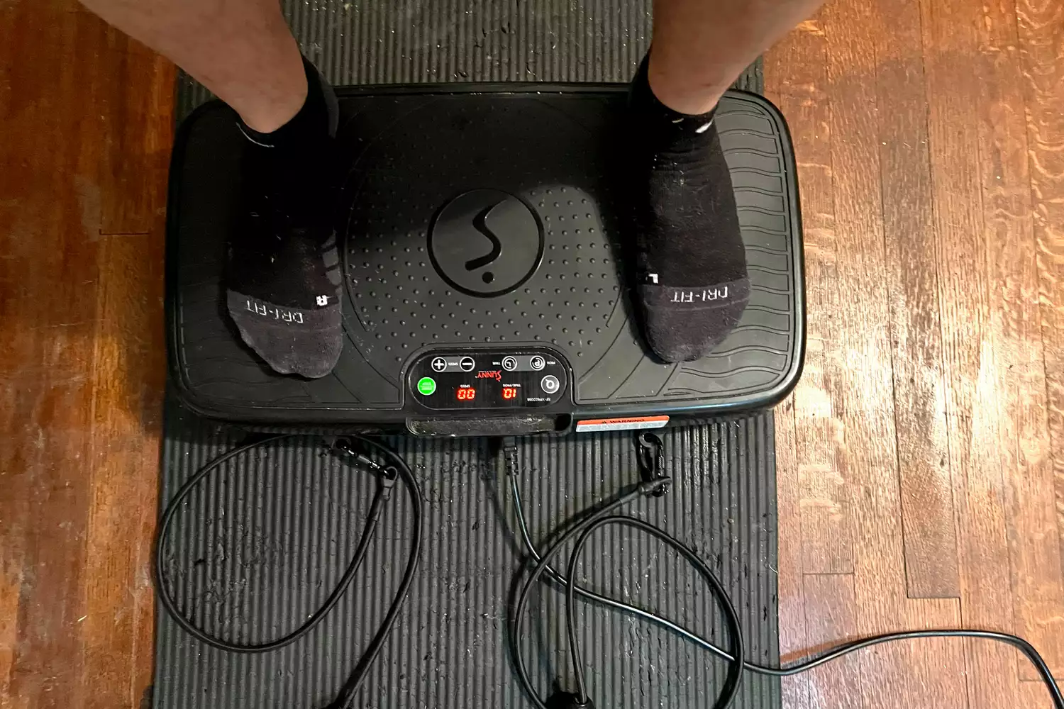 A person stands on top of the Sunny Health & Fitness Fitboard 2D Vibration Platform With Resistance Band